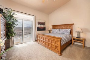 A bedroom with a wooden bed, a large window with a view, a bedside table, and a wall-mounted artwork.