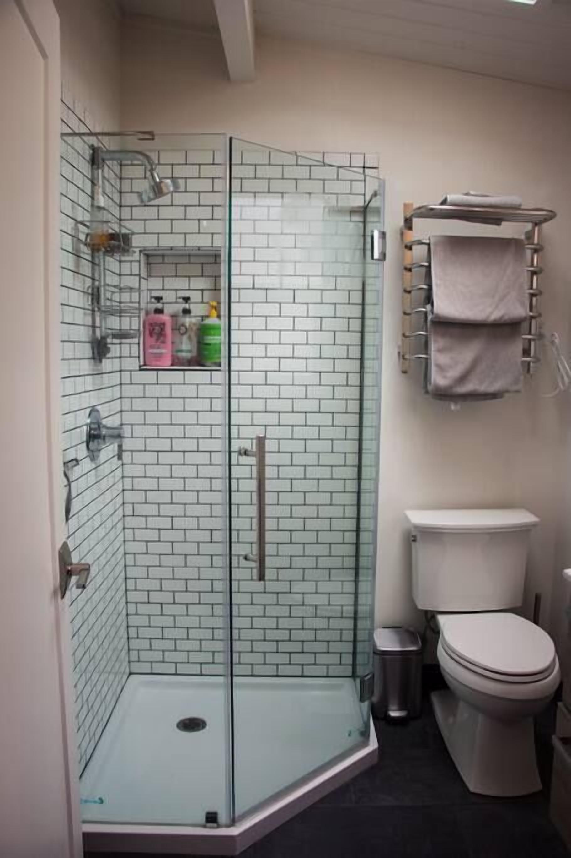 Un baño con ducha de mampara, inodoro y estante con artículos de tocador.