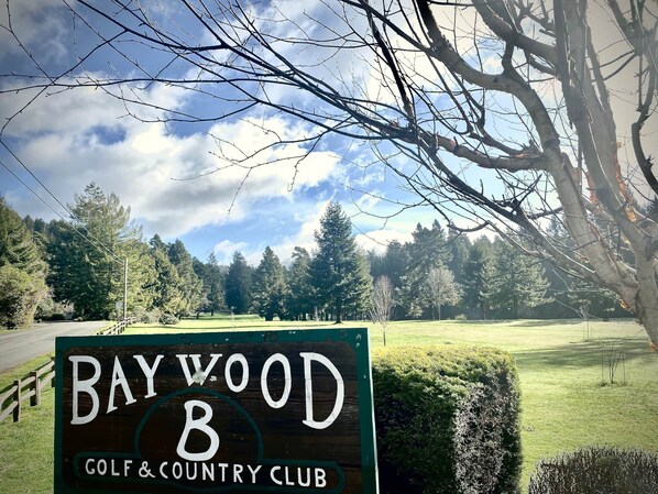 A sign for Baywood Golf & Country Club with a view of a golf course and trees in the background.