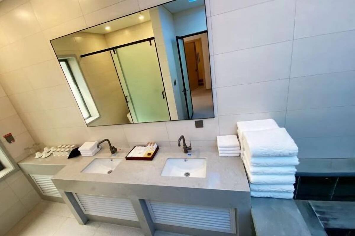 A modern bathroom with a large mirror, two sinks, and a stack of towels.
