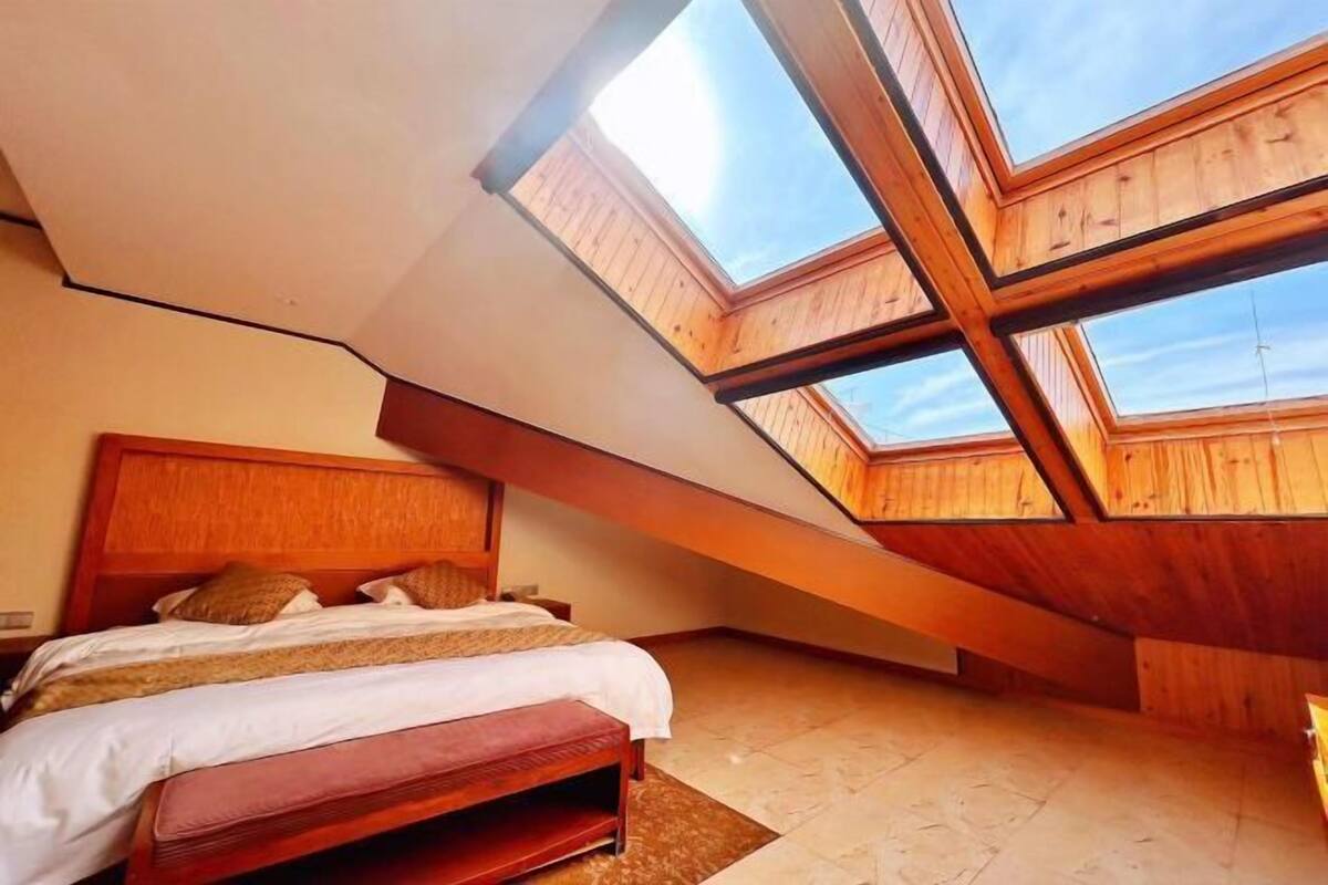 A bedroom with a skylight, wooden ceiling beams, a bed, and a bench.
