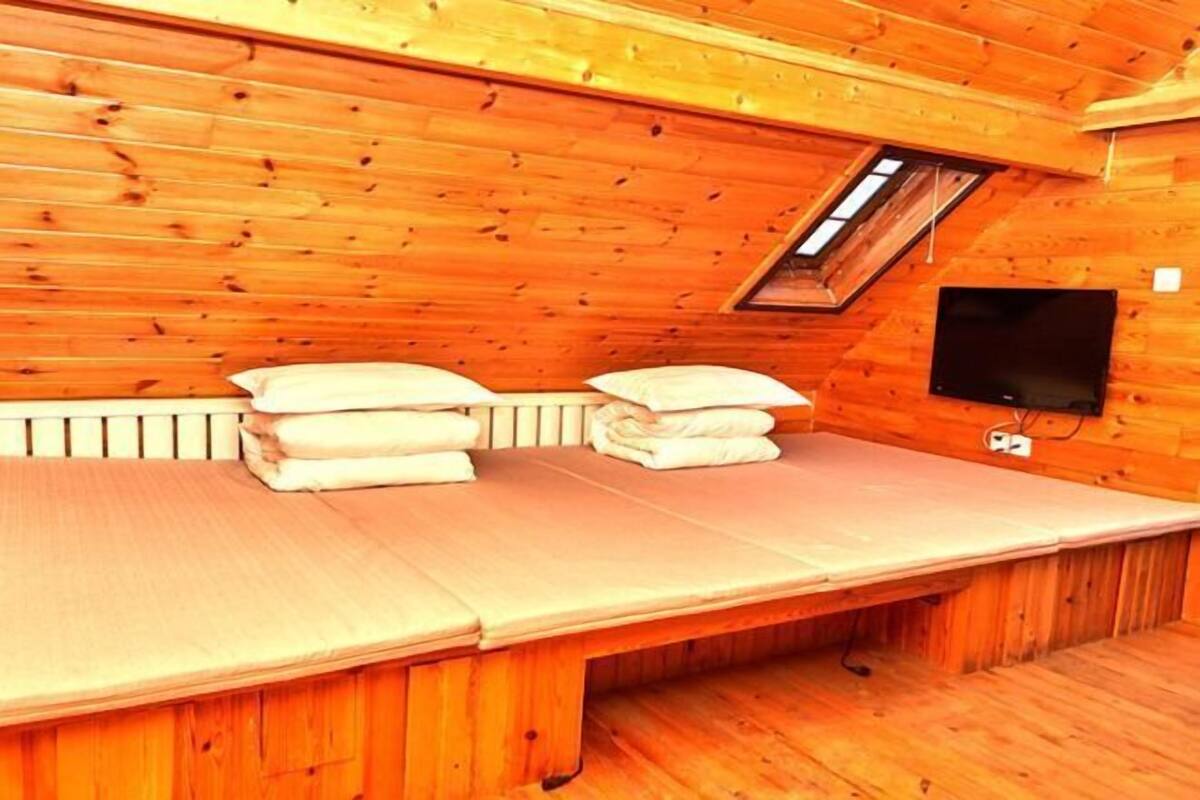 A wooden cabin room with a bed, pillows, a TV, and a skylight.