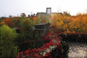 A traditional building surrounded by autumn foliage, with a stone wall and a paved area in the foreground. - Holiday Inn Hongxigu Hot Springs, Gaizhou, Yingkou (Gaizhou)