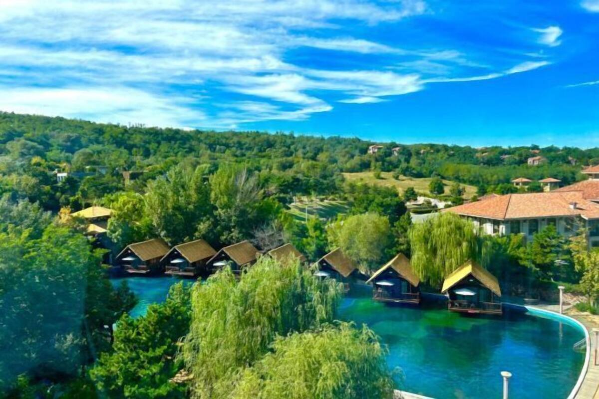 A resort with overwater bungalows, a swimming pool, and a lush green landscape.