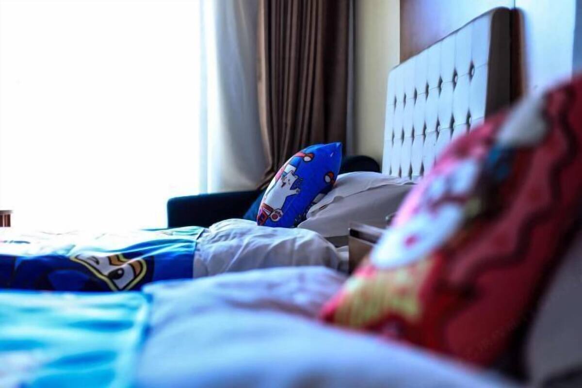 A hotel room with a bed, a headboard, and a window with curtains.