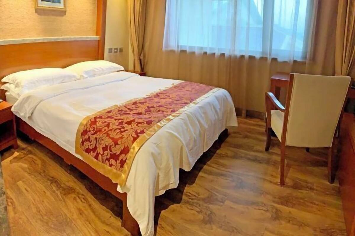 A hotel room with a wooden bed, a chair, and a window with curtains.