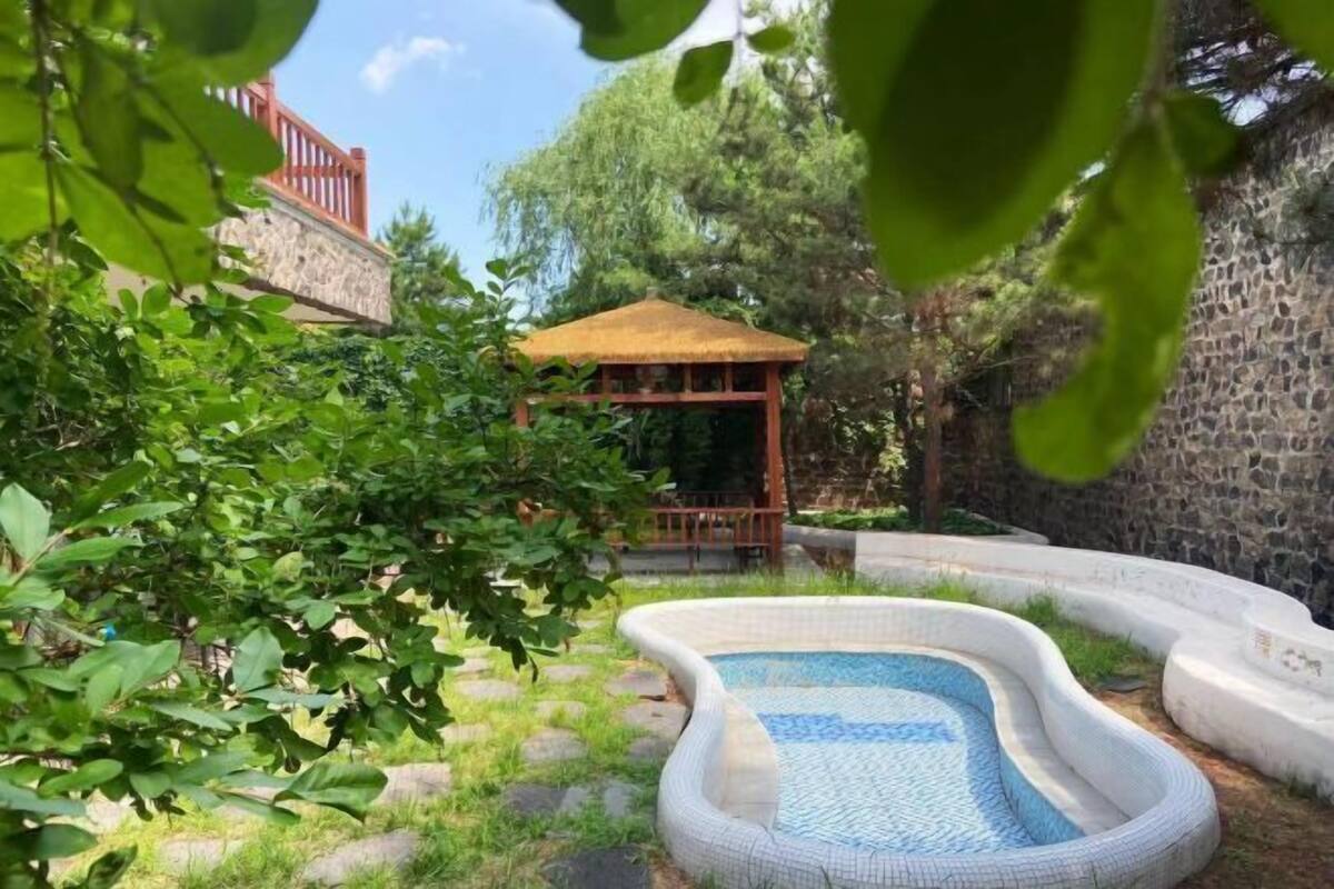 A swimming pool with a stone border, a wooden gazebo, and a stone wall.