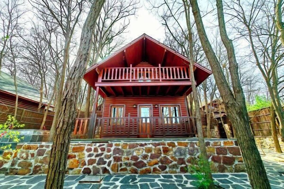 A wooden cabin with a stone foundation, surrounded by trees.