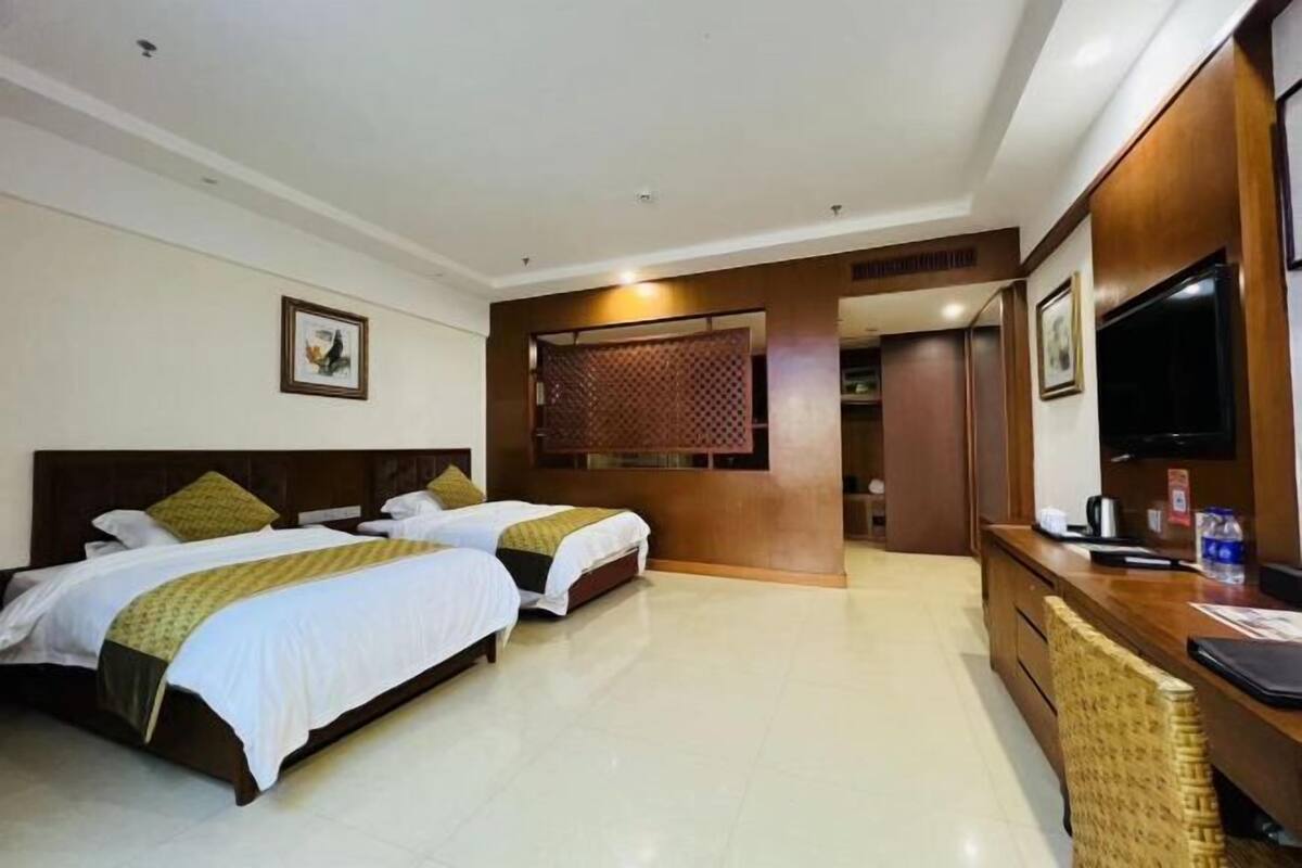 A hotel room with two beds, a desk, a television, and a decorative screen.