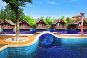 Un resort con varias piscinas, cabañas de madera y un cielo azul despejado.