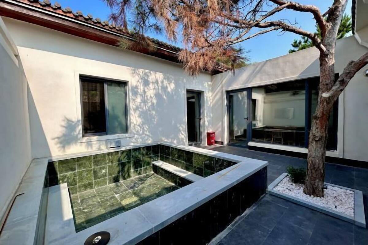 A modern house with a swimming pool, large windows, and a tree.