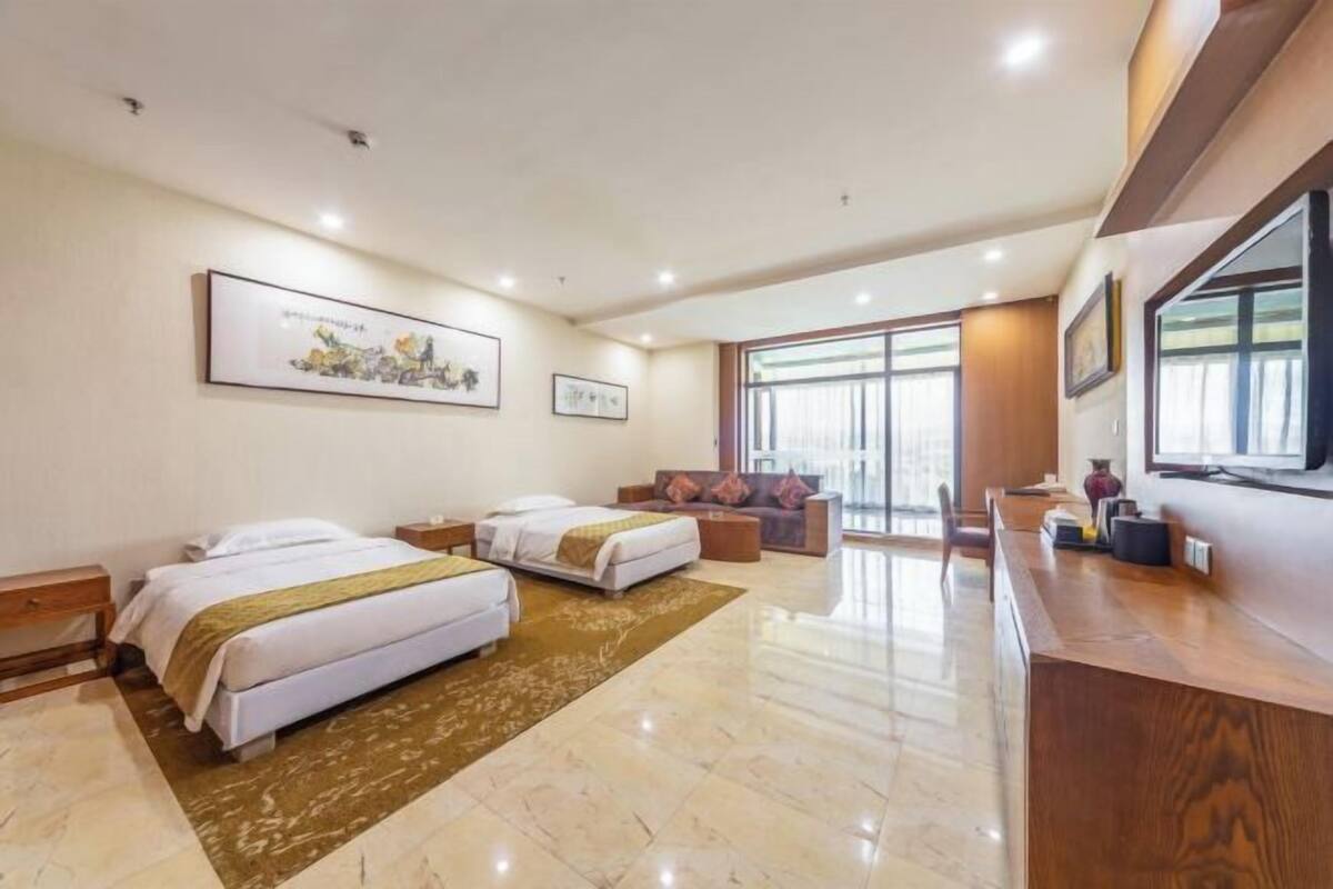 A hotel room with two beds, a sofa, a TV, and artwork on the walls.