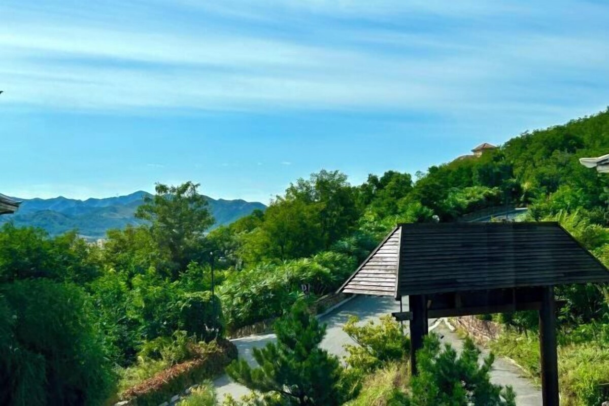 A wooden structure with a sloped roof, surrounded by lush greenery and a clear sky.