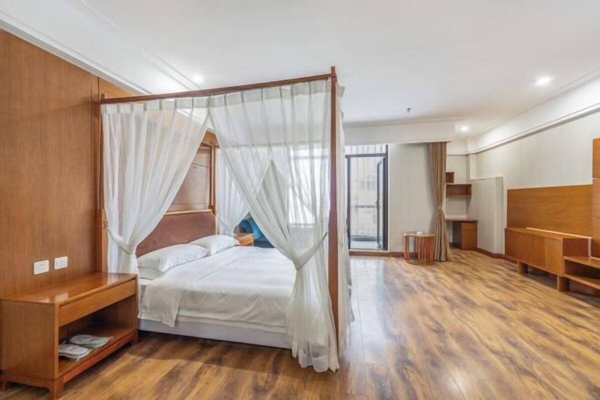 A bedroom with a four-poster bed, wooden flooring, a bedside table, and a wardrobe.