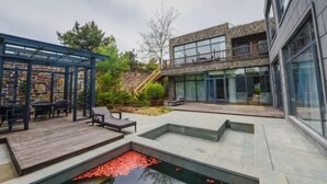 A modern outdoor patio area with a stone wall, a wooden deck, and a small pond with red flowers. - Holiday Inn Hongxigu Hot Springs, Gaizhou, Yingkou (Gaizhou)