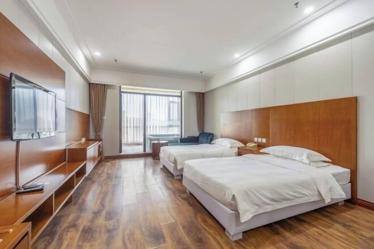 A hotel room with two beds, a TV, a desk, and a window with curtains.