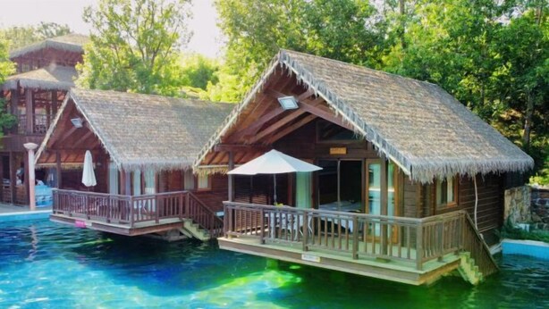 Two wooden overwater bungalows with thatched roofs, connected by a bridge, over a clear pool. - Holiday Inn Hongxigu Hot Springs, Gaizhou, Yingkou (Gaizhou)