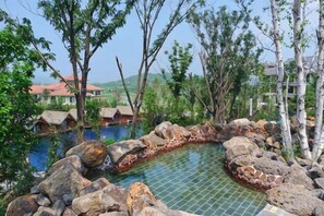A swimming pool surrounded by rocks and trees, with buildings in the background. - Holiday Inn Hongxigu Hot Springs, Gaizhou, Yingkou (Gaizhou)