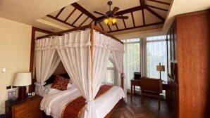 A four-poster bed with a canopy, a wooden ceiling with exposed beams, a ceiling fan, a bedside table with a lamp, and a view of the outdoors through large windows. - Holiday Inn Hongxigu Hot Springs, Gaizhou, Yingkou (Gaizhou)