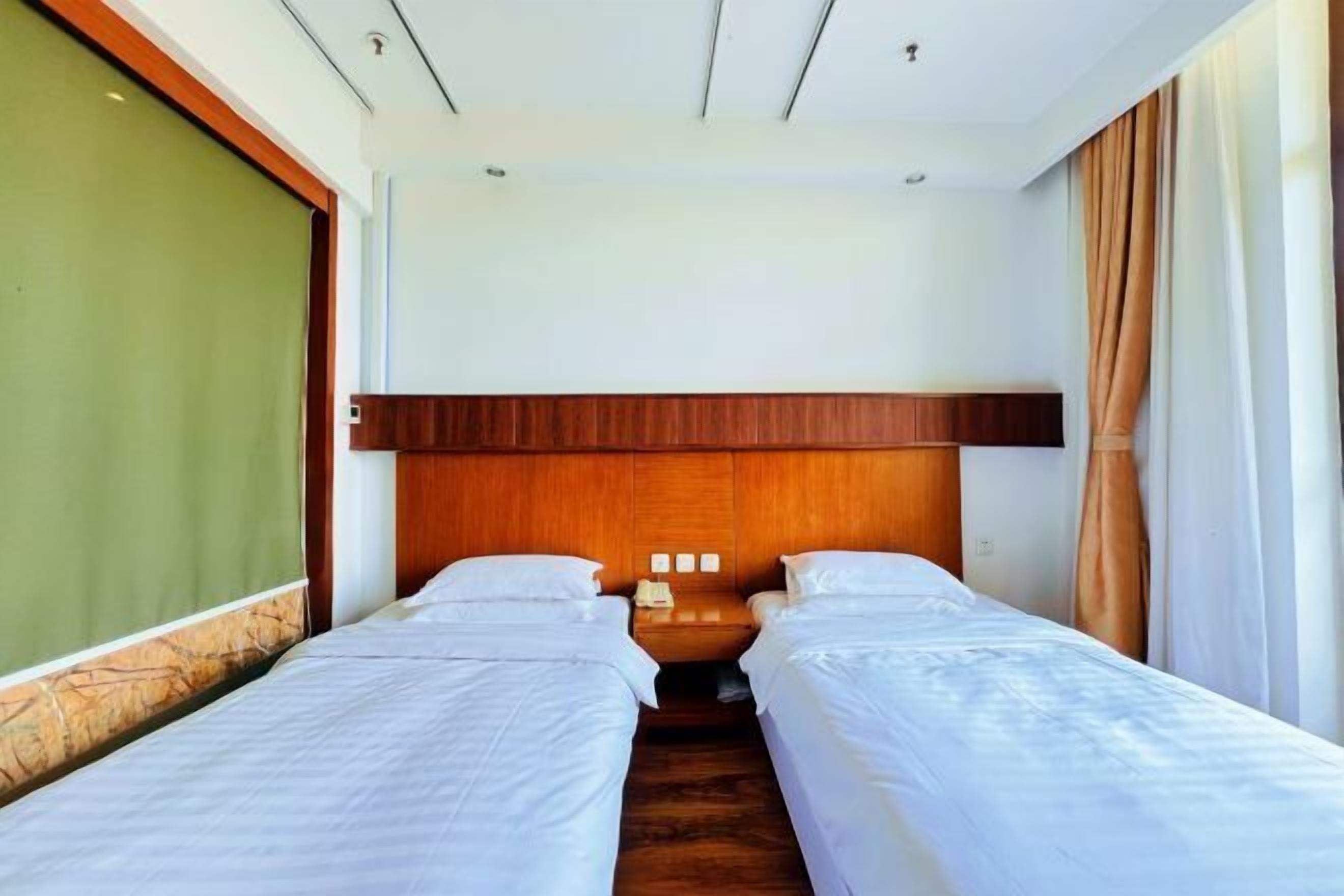 A hotel room with two single beds, a wooden headboard, a nightstand with a phone, and a green wall.