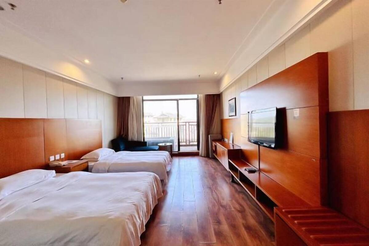 A hotel room with two beds, a TV, a wooden bench, and a balcony view.