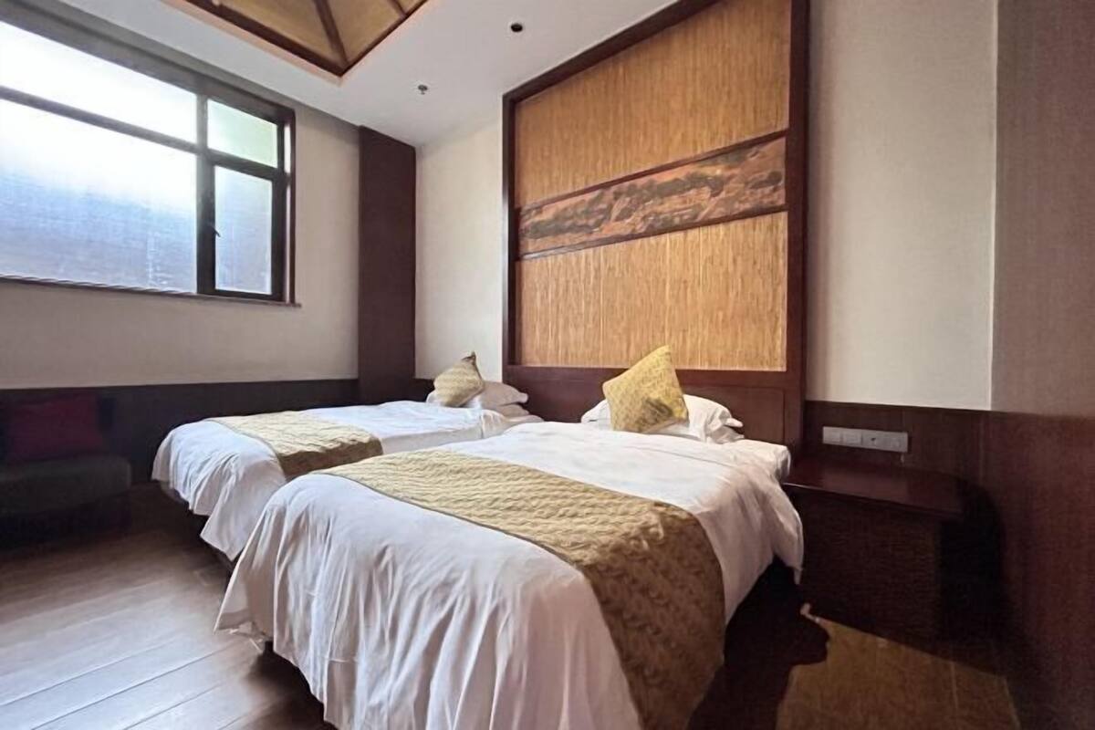 A hotel room with two beds, a large window, a wooden headboard, and a bench.