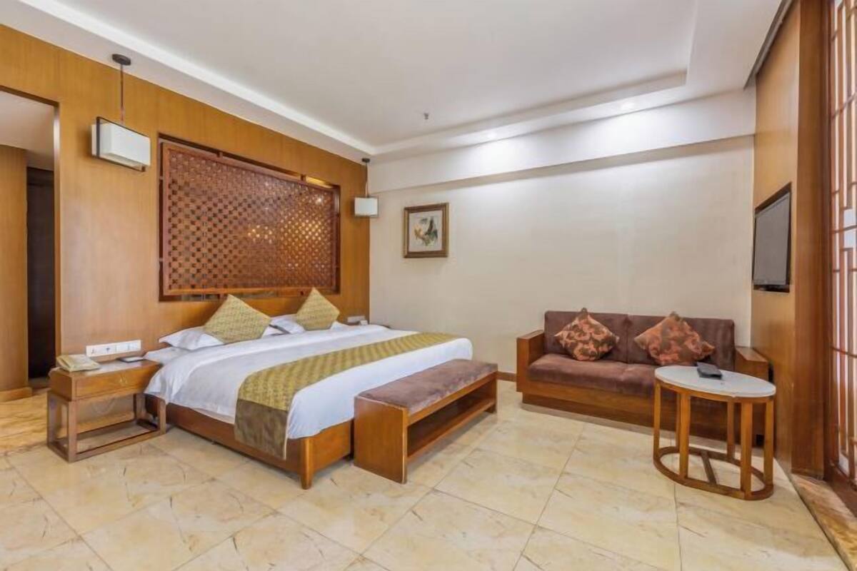A hotel room with a bed, a sofa, a small table, a TV, and a decorative screen.
