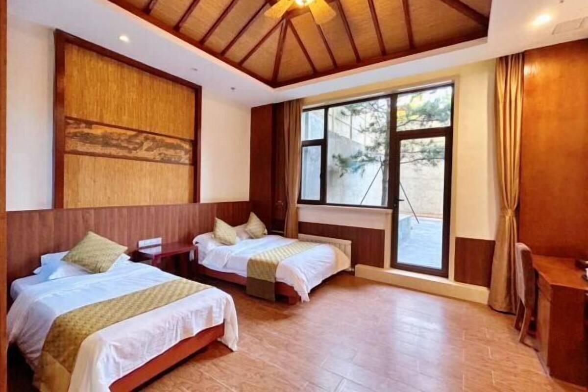A room with two beds, wooden headboards, a large window, and a ceiling fan.