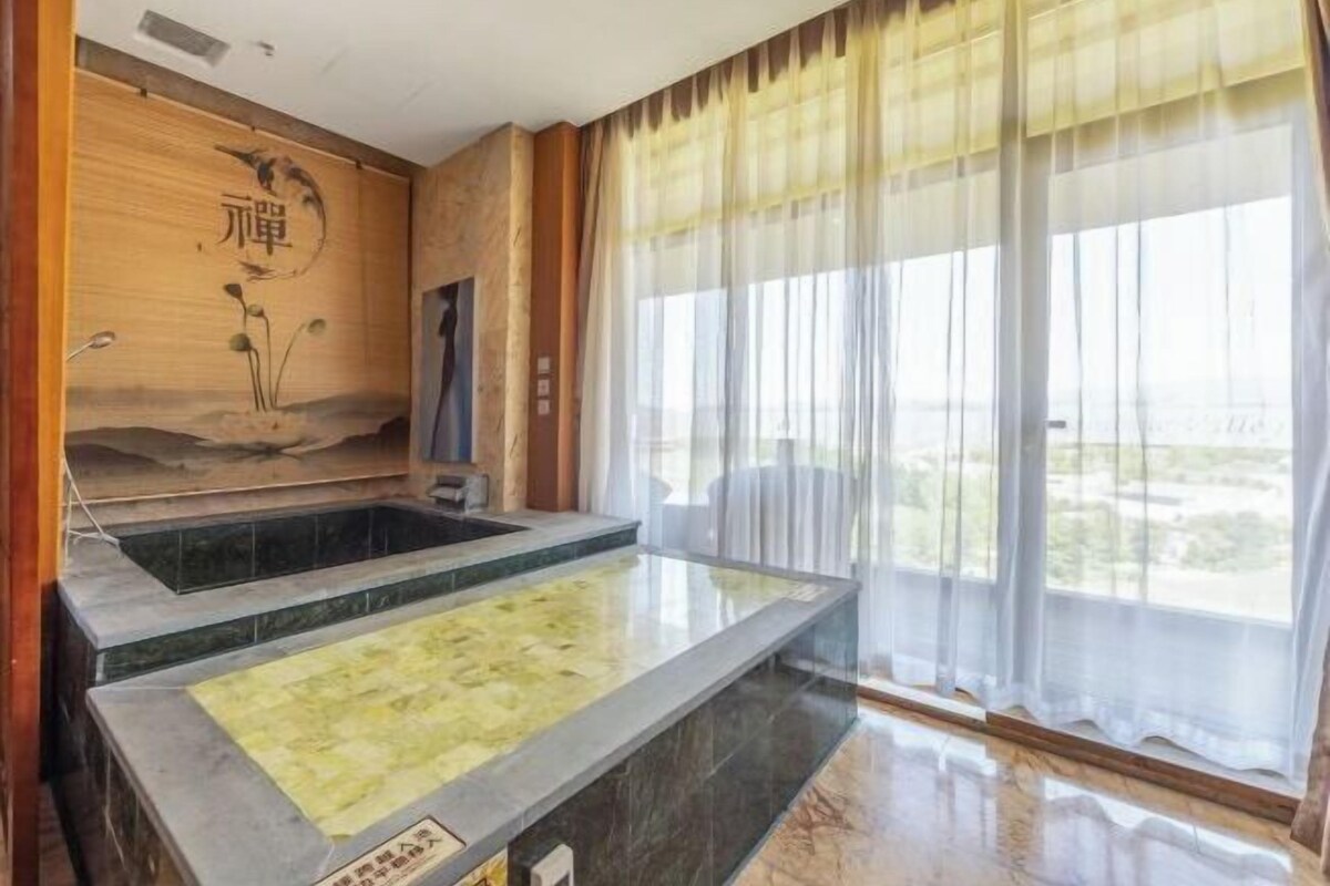 A spa area with a hot tub, a wooden wall with artwork, and a large window with sheer curtains.