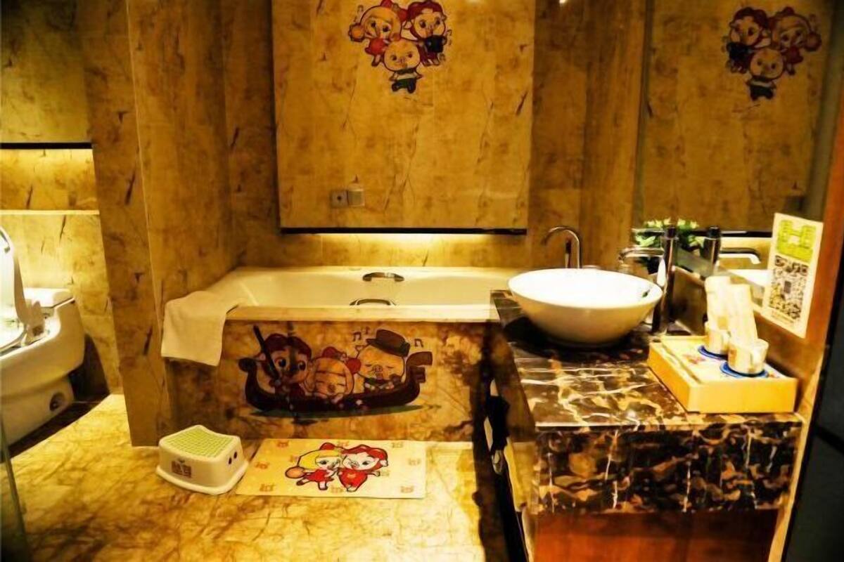 A bathroom with a bathtub, a sink, and a toilet. There are cartoon characters on the walls and a small mat on the floor.