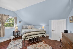 Une chambre à coucher comprenant un lit, une commode, une table de chevet, une lampe, une fenêtre avec des rideaux et une porte.