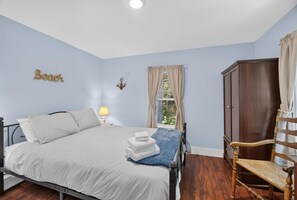 A bedroom with a bed, a chair, a wardrobe, and a window with curtains. - Recently Renovated Home Minutes from Ocean Point (Boothbay)