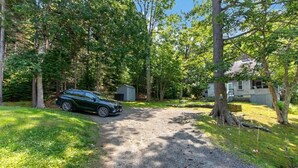 Une allée de gravier mène à une maison entourée d’arbres.