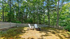 Une cour arrière clôturée avec une pelouse, deux fauteuils Adirondack et une petite table.