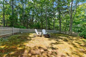 Ein umzäunter Garten mit Rasenfläche, zwei Adirondack-Stühlen und einem kleinen Tisch.