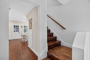 Un escalier avec des marches en bois et une rampe blanche, menant à une pièce dotée d’une porte blanche et d’une fenêtre.