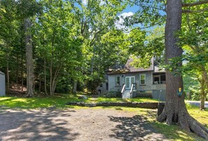 Une maison avec un porche à l’avant, entourée d’arbres et donnant sur une allée gravillonnée.