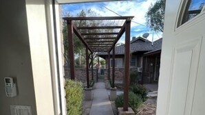 A covered walkway leading to a house with a stone facade, a satellite dish, and a visible outdoor area with plants. - West University Carriage Home & Parking (Tucson)