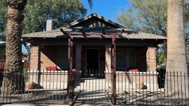A building with a wooden porch, brick walls, and a metal fence. - West University Carriage Home & Parking (Tucson)