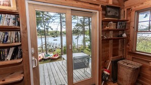 Une cabane en bois dotée d’une porte-fenêtre coulissante donnant sur une terrasse où se trouvent des canoës, une table et des chaises.