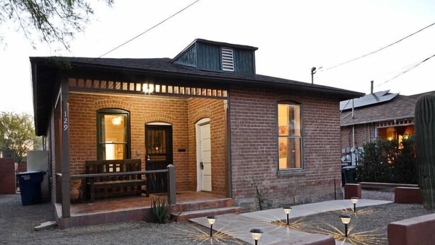 Een bakstenen huis met een veranda, een voordeur en een kleine tuin met sfeerverlichting.