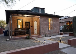 Una casa de ladrillo con un porche, una puerta principal y un pequeño jardín decorado con luces.