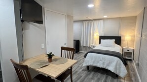 Ein Zimmer mit einem Bett, einem Nachttisch, einer Lampe und einem an der Wand befestigten Fernseher.