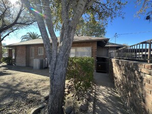 A residential house with a brick exterior, a garage, and a small garden area with a tree and shrubs.