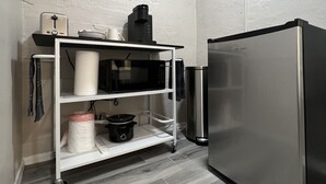 Eine kompakte Küche mit Edelstahlkühlschrank, Mikrowelle, Kaffeemaschine und einem kleinen Wagen mit Küchenutensilien.