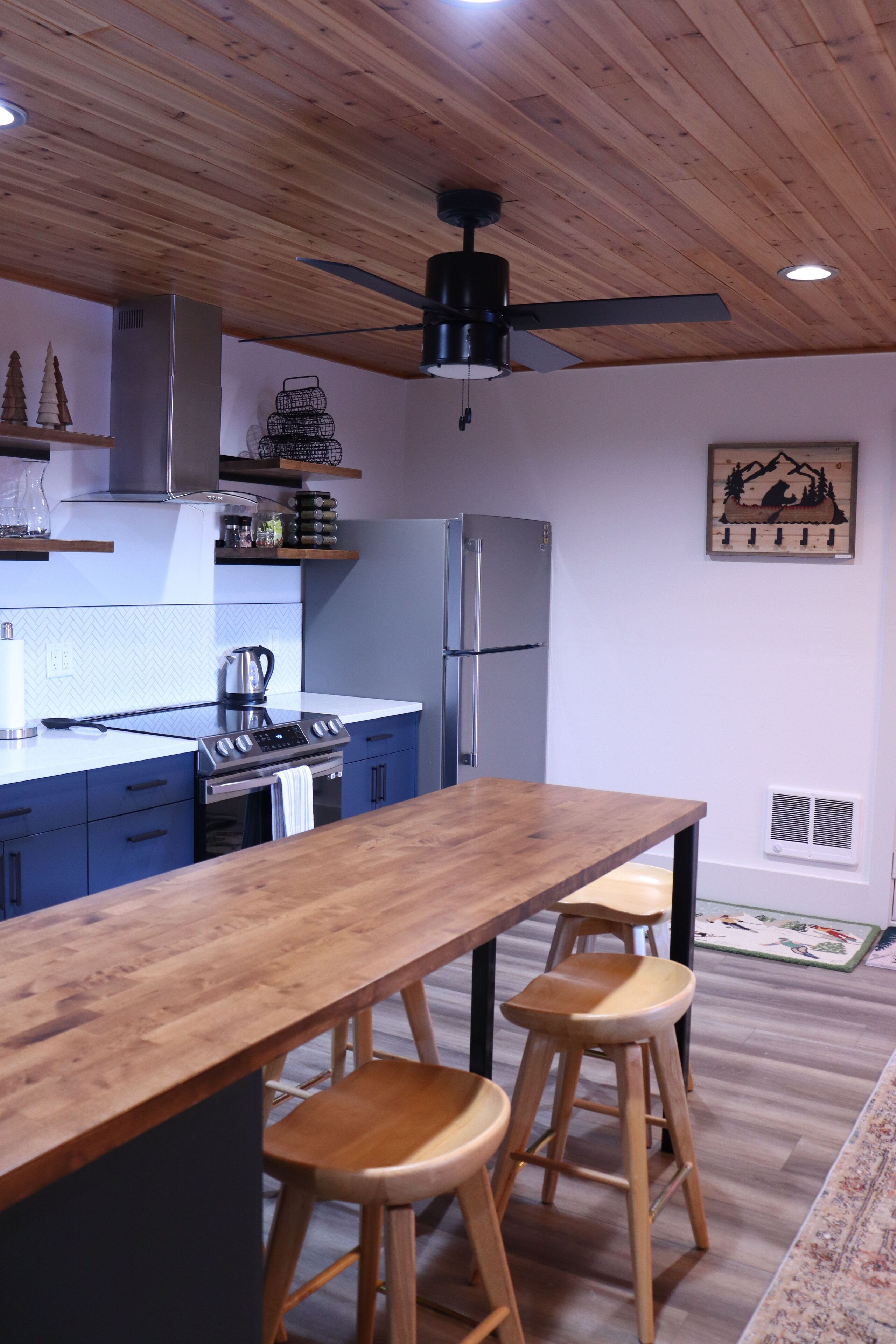 Une cuisine moderne avec un plafond en bois, un îlot central doté de tabourets, des appareils en acier inoxydable et des objets décoratifs disposés sur des étagères.