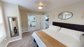 A bedroom with a large bed, a ceiling fan, a mirror, and a view into the bathroom and kitchen.