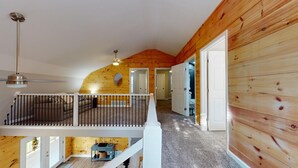 A spacious loft bedroom with a high ceiling, wooden walls, a balcony, and a modern chandelier.