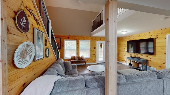 A cozy living room with a gray sectional sofa, a small round table, and a TV mounted on the wall.