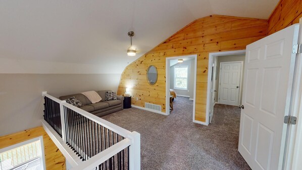 A loft-style room with a sloped ceiling, a wooden wall, a sofa, a small table, and a door leading to another room. - Secluded modern cabin, with hot tub (Logan)